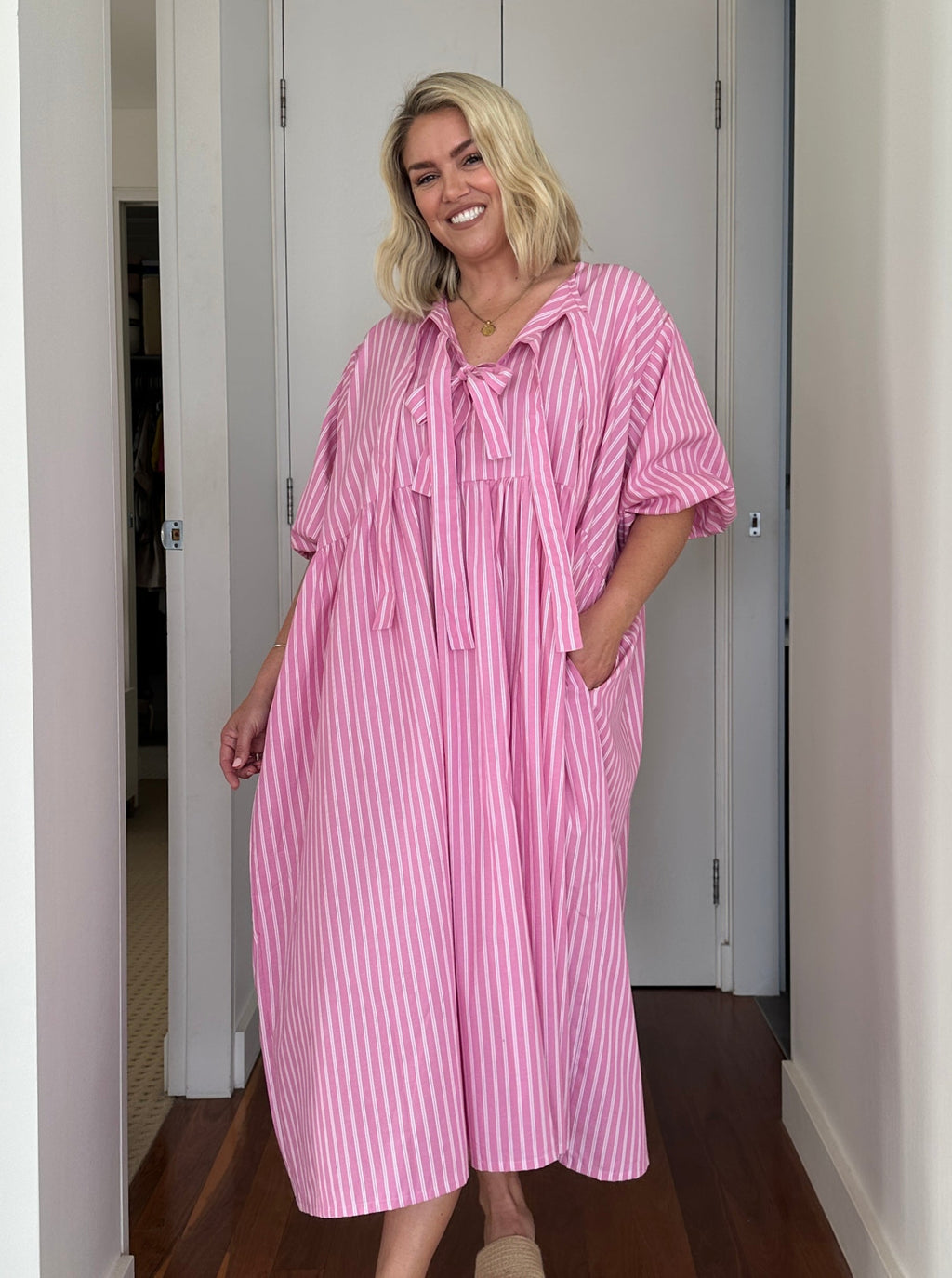Woman wearing a pink and white striped dress standing in a doorway.
