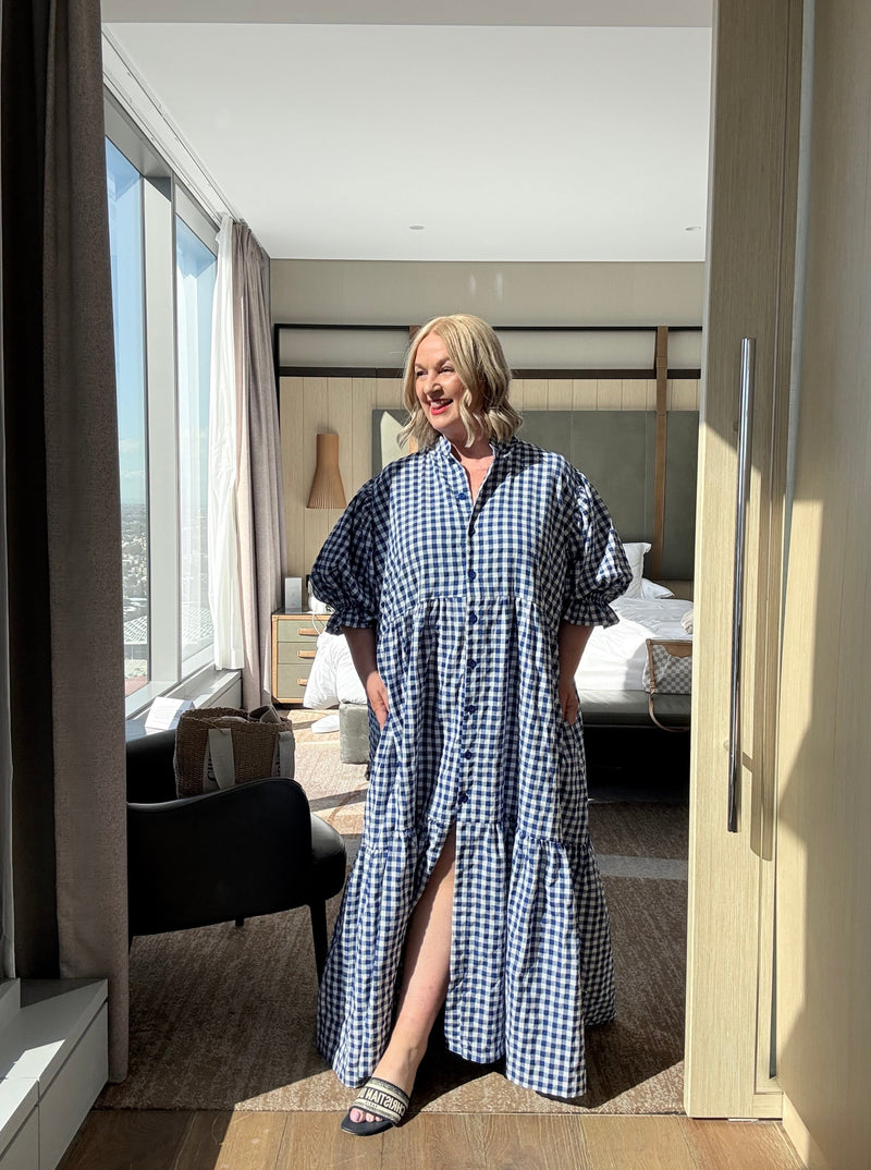 Person wearing a blue and white checkered dress standing in a room with a skylight.