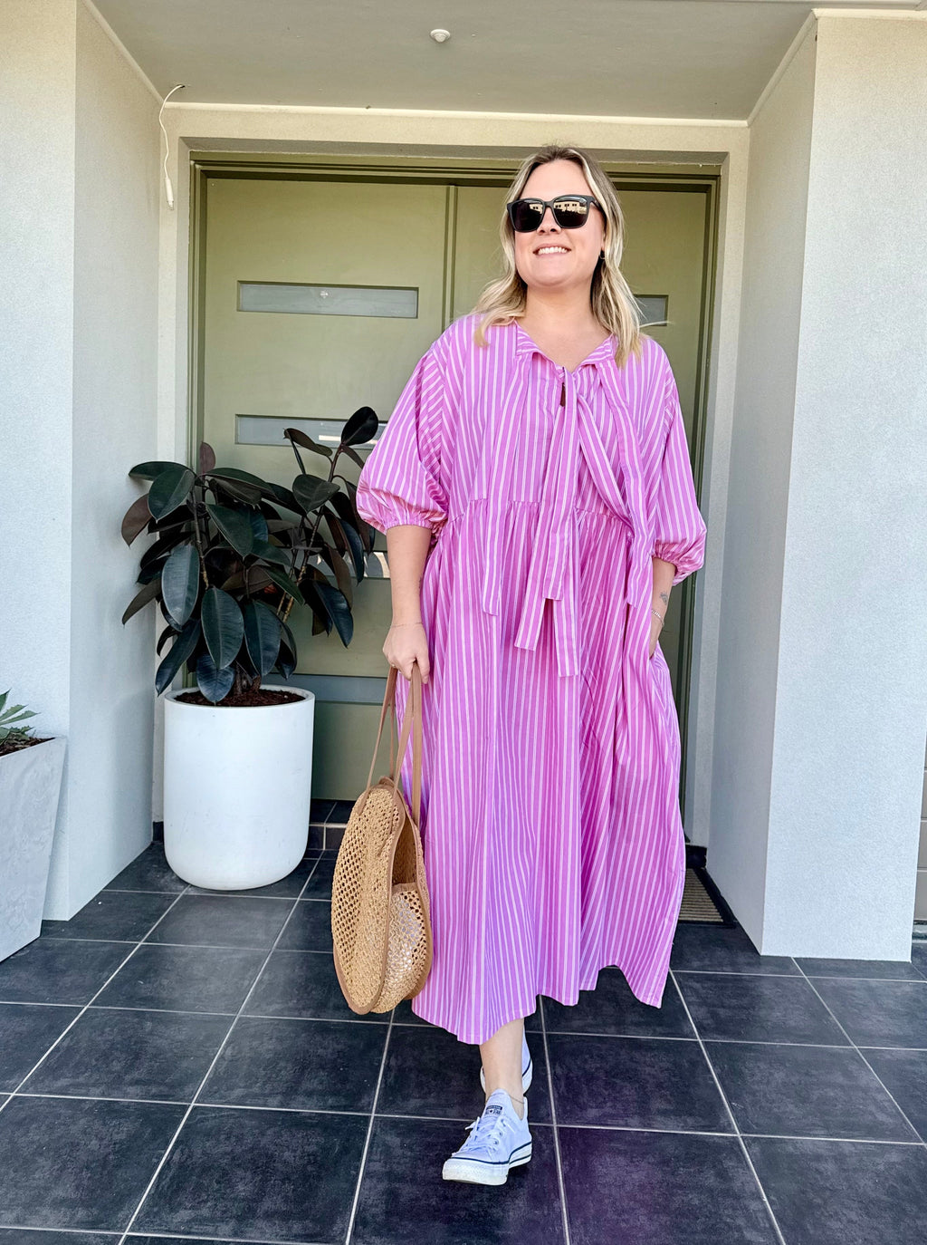 Woman in a pink dress standing outside a building with a plant in the background